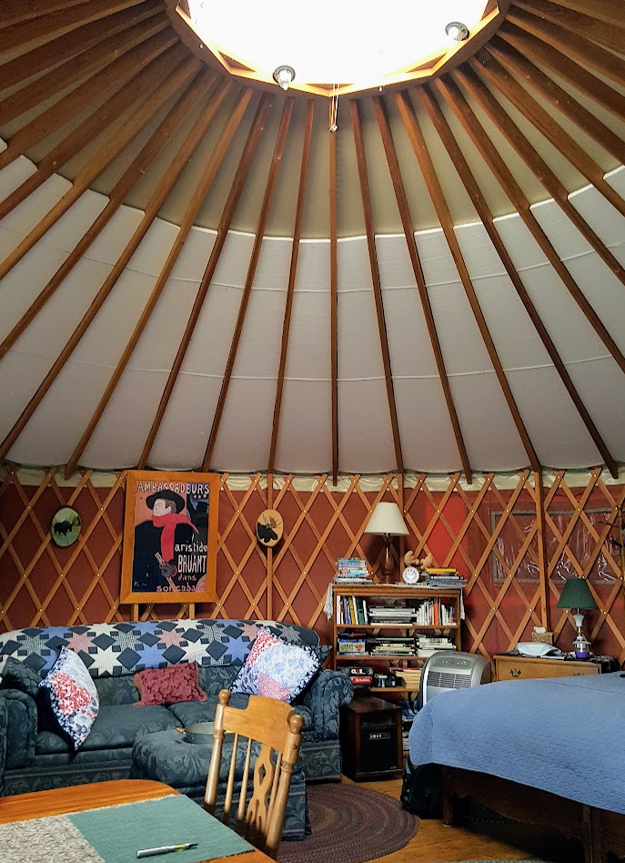 Inside of yurt with a couhc, bed, and table